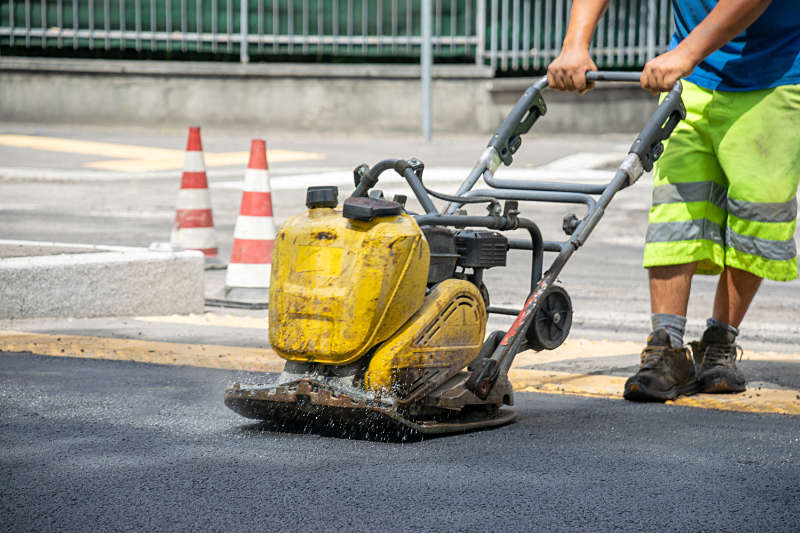 Bauarbeiter verdichtet Asphaltschicht auf Straße